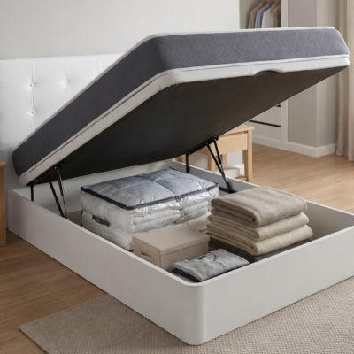 Canapé abatible de madera blanca "Americ" abierto en un dormitorio, mostrando su gran capacidad de almacenaje interior con mantas, ropa de cama y cajas organizadas. El colchón está elevado por los pistones hidráulicos. Ideal para ganar espacio.