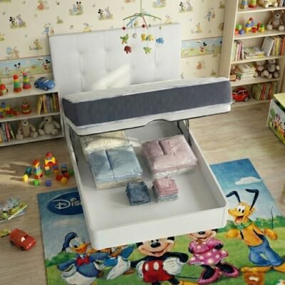 "Vista aérea de canapé abatible infantil blanco abierto mostrando su gran capacidad de almacenaje interior con ropa de cama organizada, situado en una habitación juvenil con alfombra de Mickey Mouse y estantería de juguetes."
